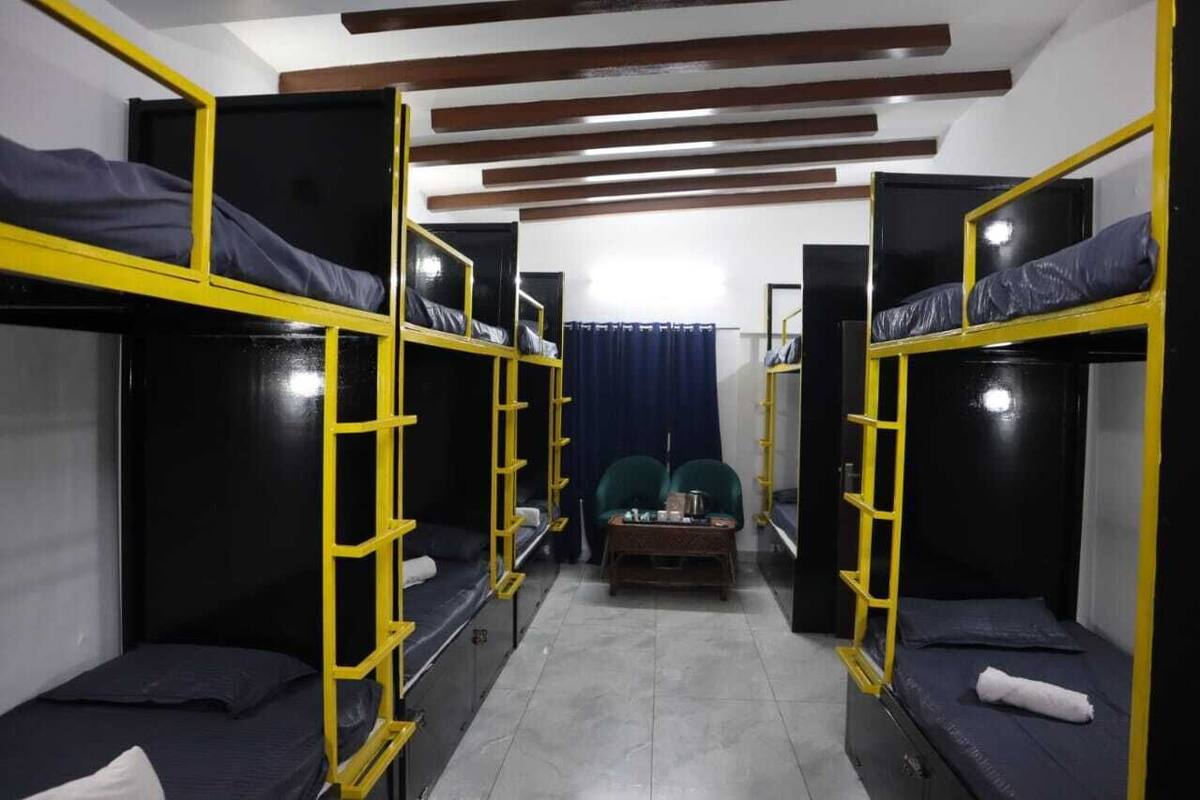A dormitory room with bunk beds, a small table, and a curtain.