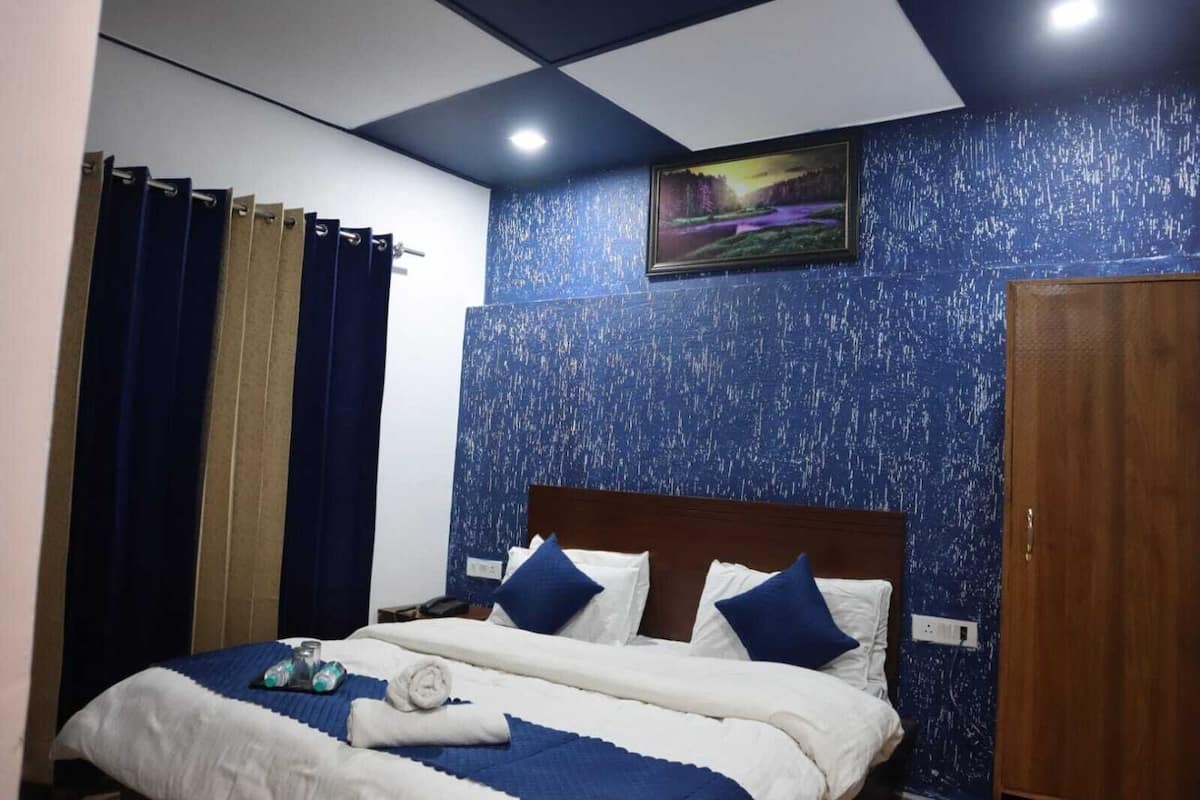 A hotel room with a bed, curtains, a painting, and a wooden wardrobe.