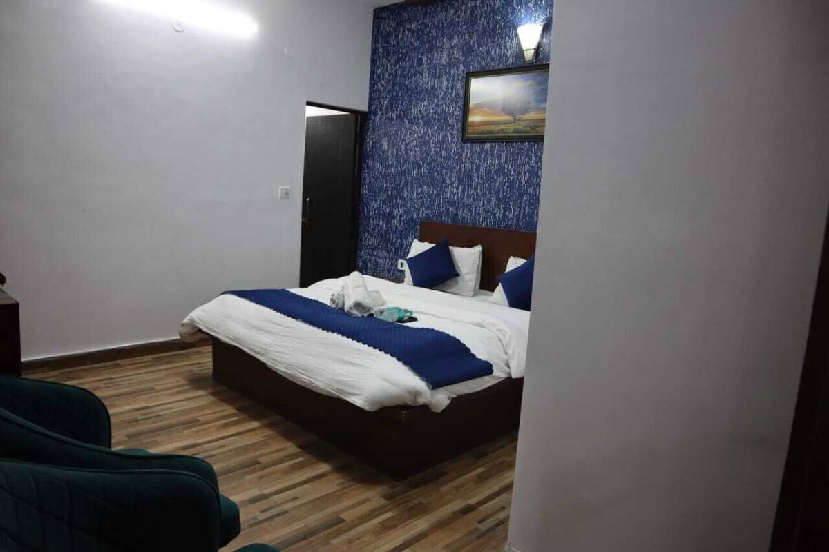 A bedroom with a wooden floor, a bed with white and blue bedding, a dark headboard, and a blue textured wall with a picture.
