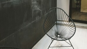 Un interior moderno con dos sillas de estructura metálica negra, una pared oscura con textura y una puerta de cristal que da a otra habitación.