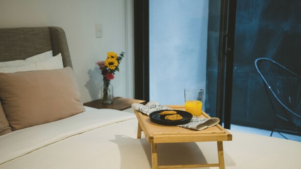 Una cama con una mesita de noche de madera que sostiene un plato de galletas y un vaso de jugo de naranja.