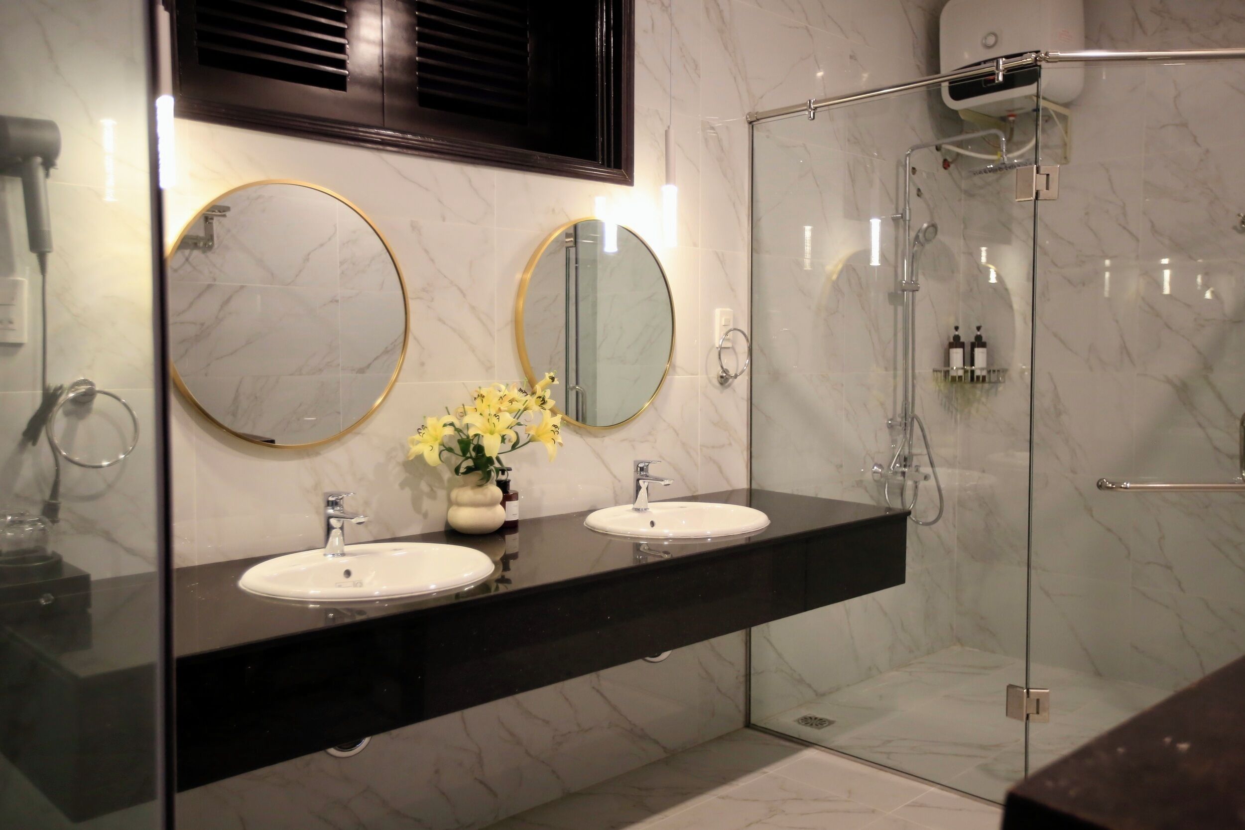 A modern bathroom with two sinks, a glass-enclosed shower, and marble walls.