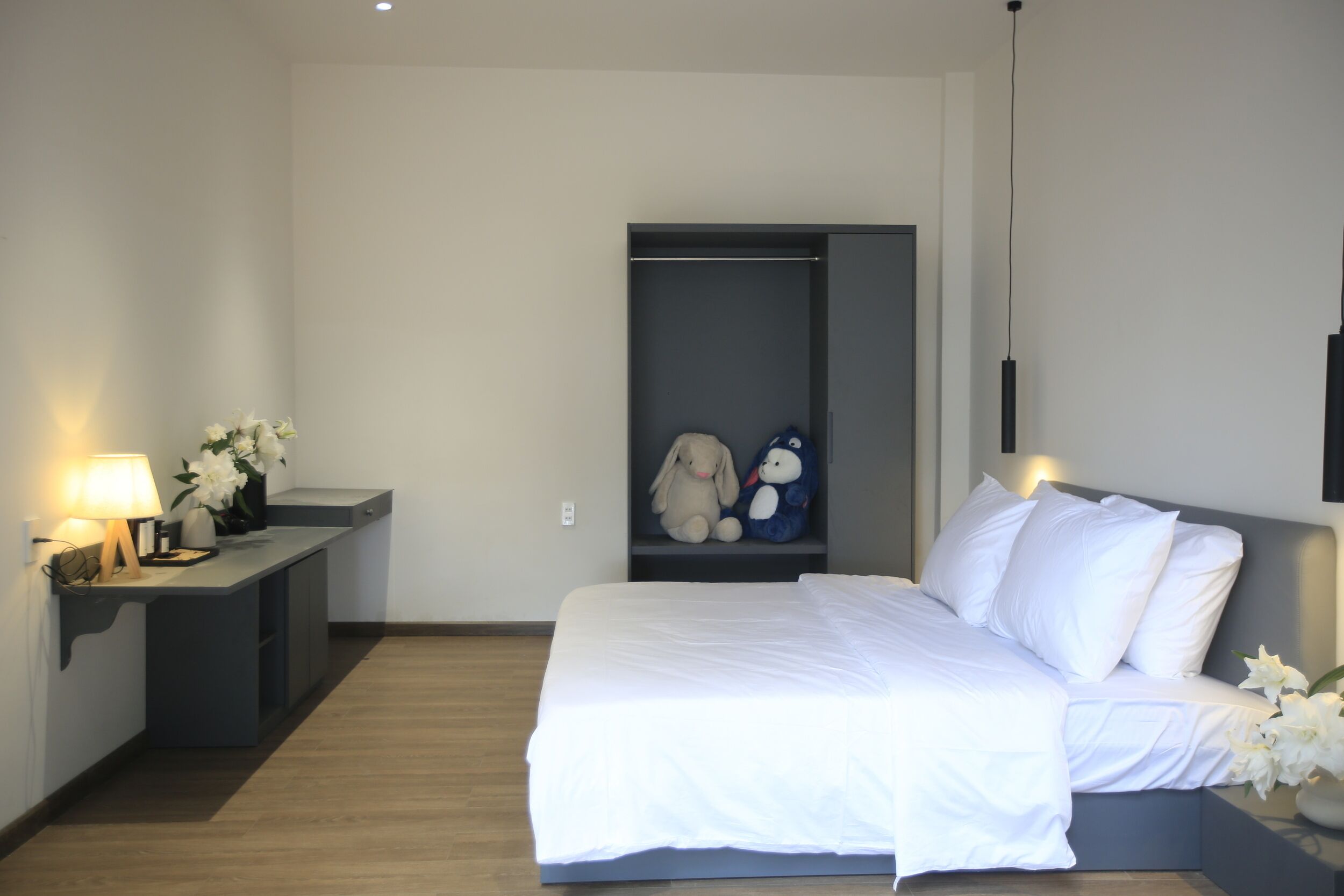 Une chambre à coucher avec un lit, une table de chevet avec une lampe et une étagère avec des peluches.