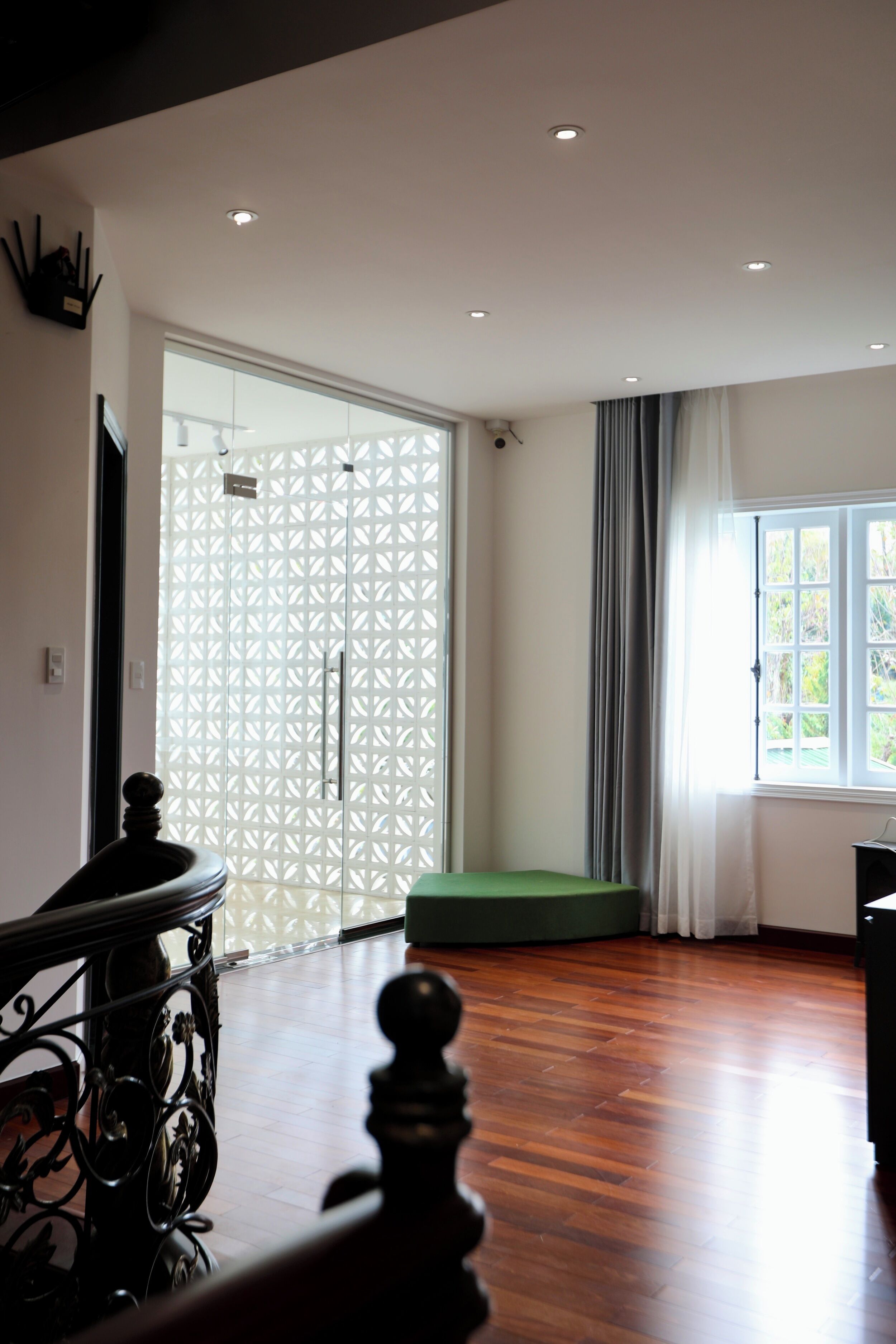 Ein Zimmer mit Holzboden, einem grünen Sofa, einem schwarzen Metallgeländer und einem Fenster mit Vorhängen.