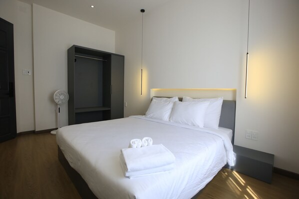 A neatly made bed with white linens, a bedside table, and a wall-mounted light fixture. - DD Hospitality - May Bach Da Lat (Lam Vien - Da Lat)