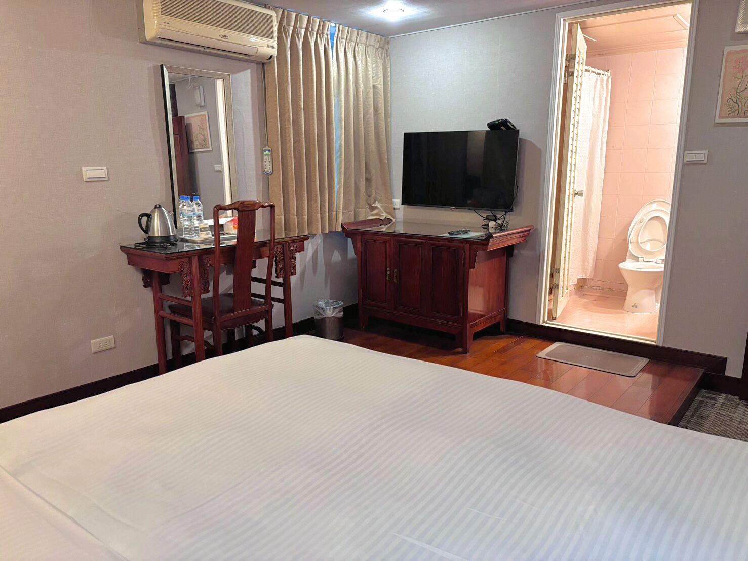 A hotel room with a bed, a desk with a chair, a television, and a bathroom visible through an open door.
