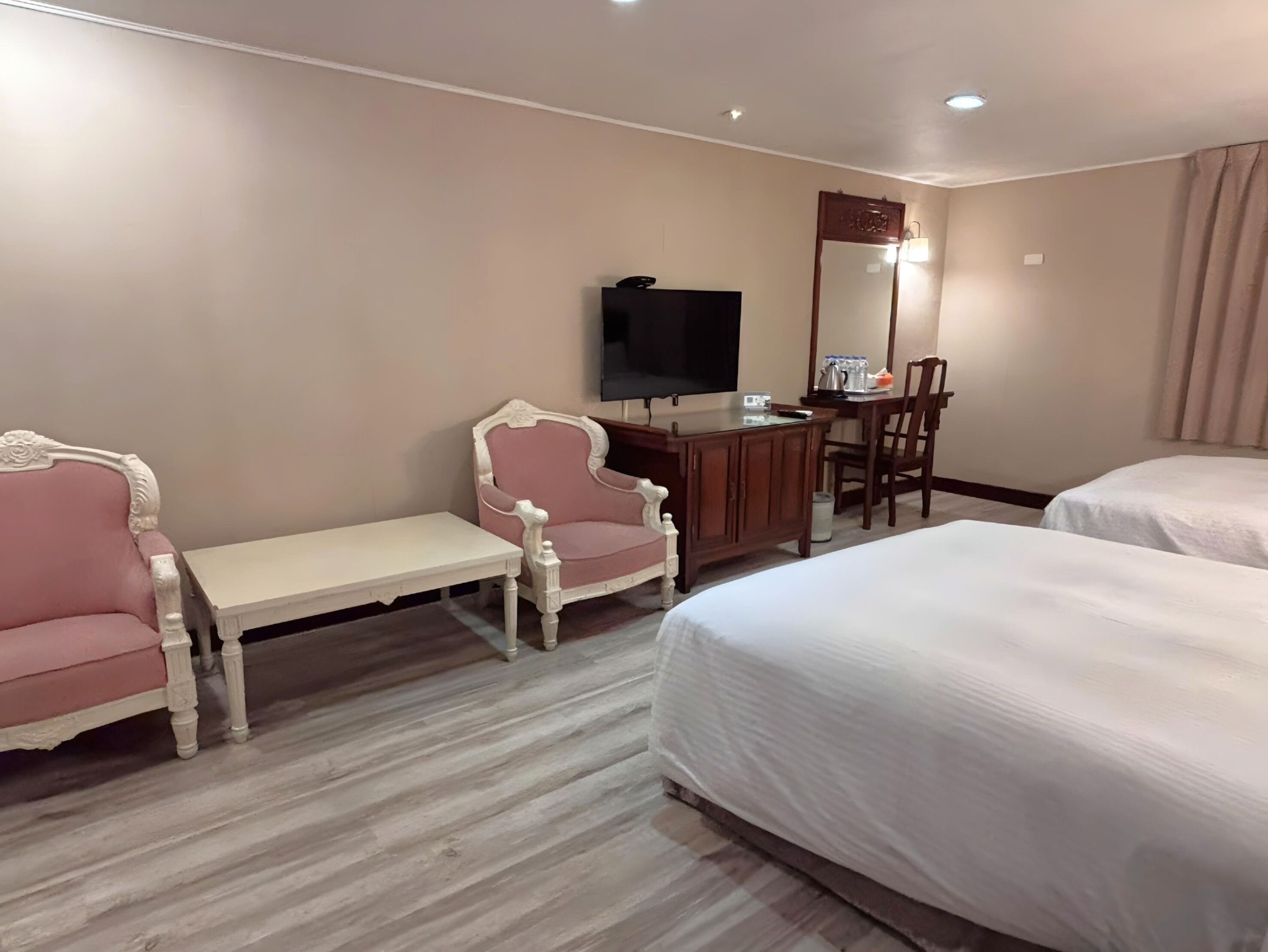 A hotel room with two beds, a desk with a TV, a chair, and a small table.