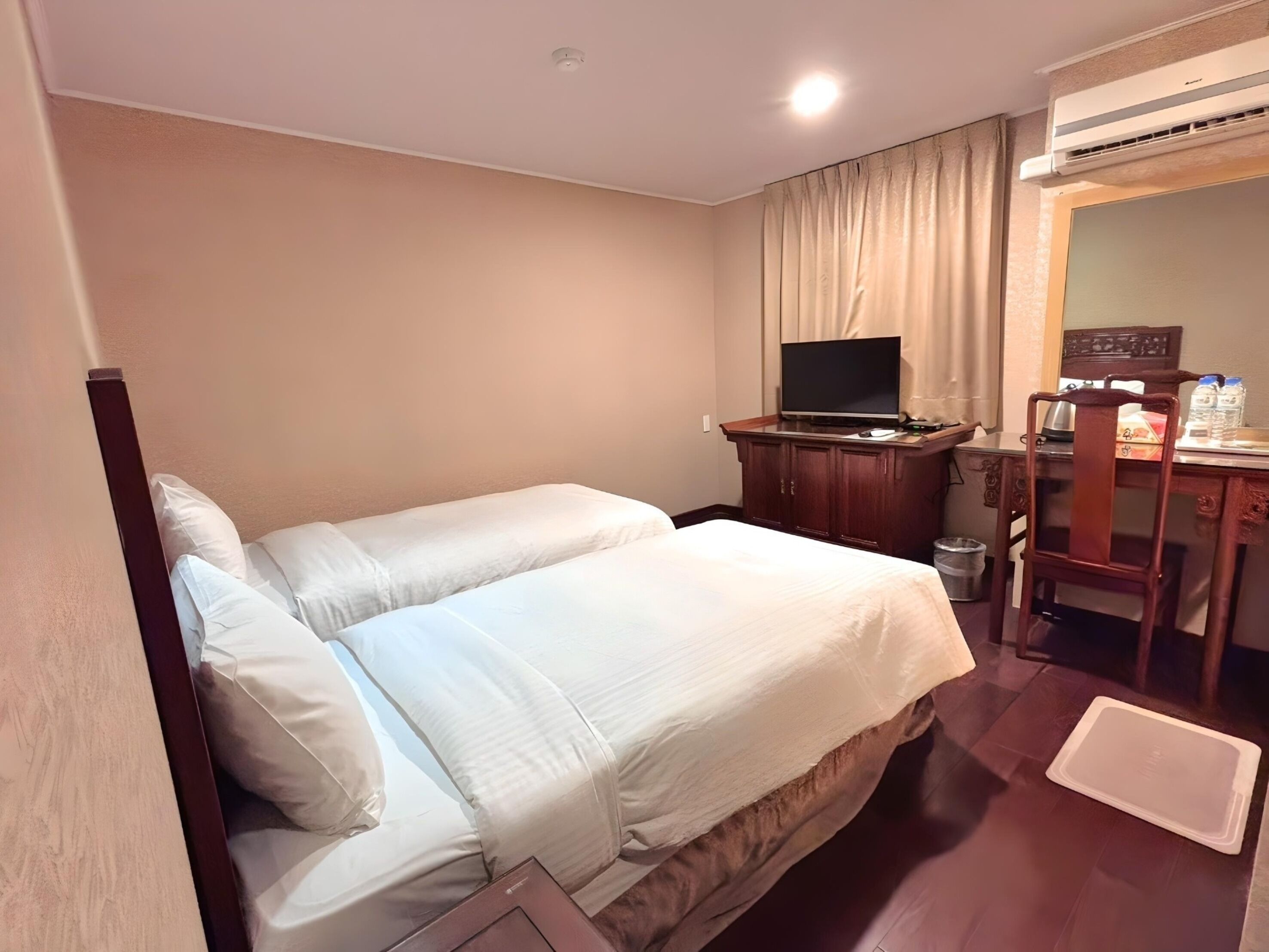 A hotel room with a bed, a desk, a television, and an air conditioning unit.