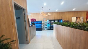 Uma área de recepção de hotel com um balcão de madeira, um balcão azul e um refrigerador cheio de bebidas.