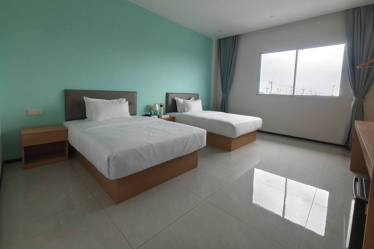 A hotel room with two beds, a window with a city view, and a tiled floor.