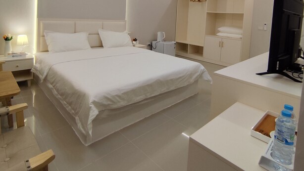 Quarto de hotel moderno com uma cama grande, mesas de cabeceira, escrivaninha, guarda-roupa e televisão.