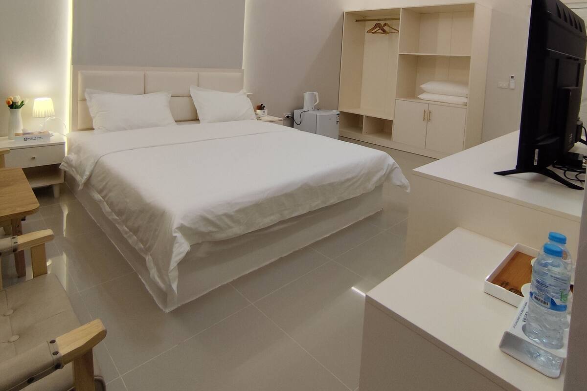 A modern hotel room with a large bed, bedside tables, a desk, a wardrobe, and a television.