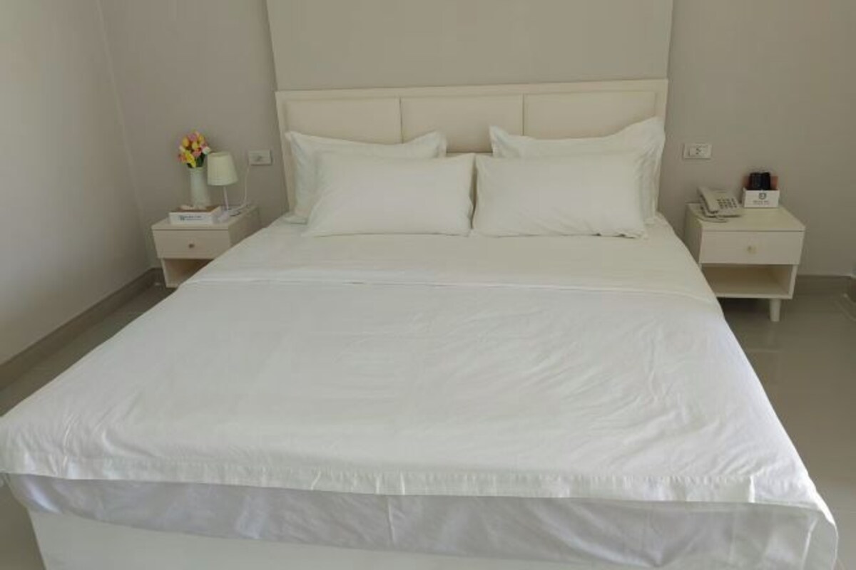 A neatly made bed with white linens and pillows, two bedside tables with lamps and a phone, and a vase with flowers on one table.
