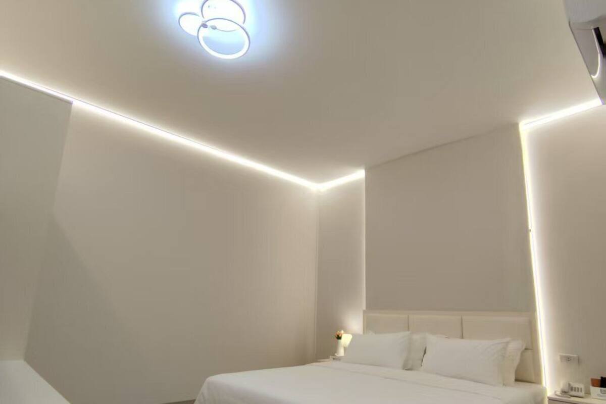 A modern hotel room with a large bed, bedside tables, and a ceiling light fixture.