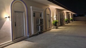 Corredor de hotel com portas em arco, unidades de ar condicionado e plantas em vasos.