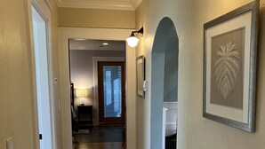 Un couloir doté d’un plancher en bois, une porte avec un panneau en verre dépoli et un luminaire fixé au mur.