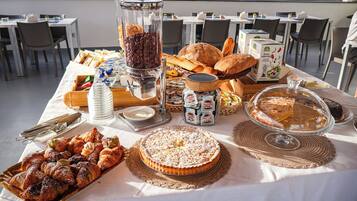 Una mesa de buffet con diversas opciones de repostería, incluyendo pasteles y pan, además de una estación de café.