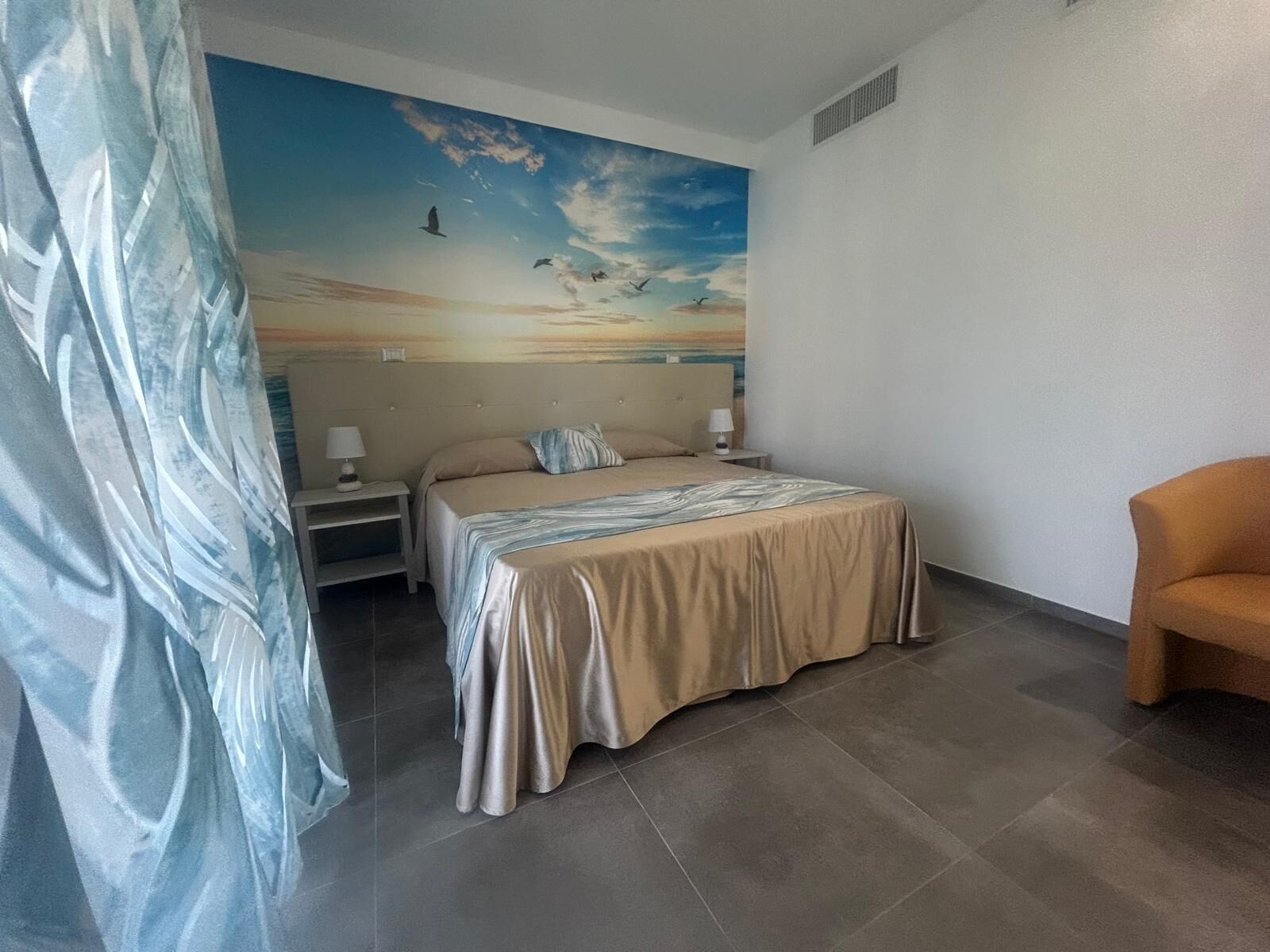 Une chambre à coucher avec un lit, des tables de chevet, une chaise, une fresque murale et un rideau.