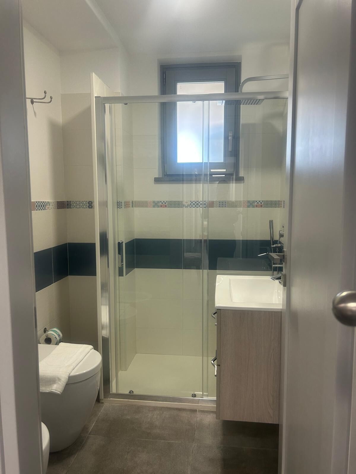 Un baño moderno con cabina de ducha de vidrio, inodoro y lavamanos con mueble de madera.