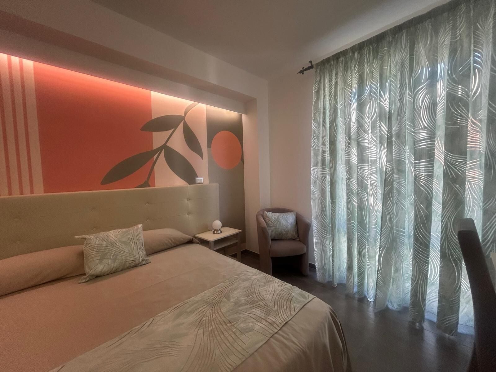 Ein modernes Hotelzimmer mit einem großen Bett, einem Nachttisch, einem Sessel und einer Wand mit einem Blattmuster.