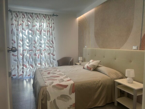 A hotel room with a bed, a nightstand, a chair, and a curtain with a leaf pattern. - Eolia Rooms Lipari (Lipari)