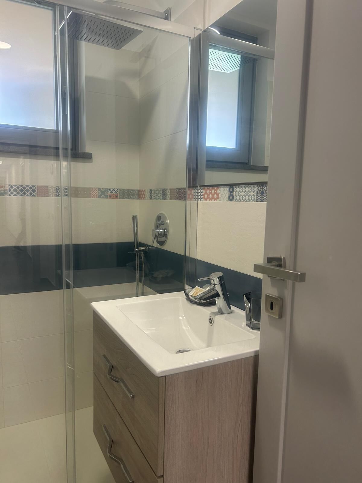 A modern bathroom with a glass shower enclosure, a white sink, and a wooden cabinet.