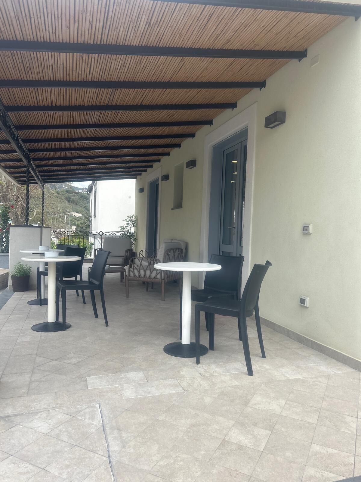 An outdoor patio with tiled flooring and covered seating areas, including tables and chairs.