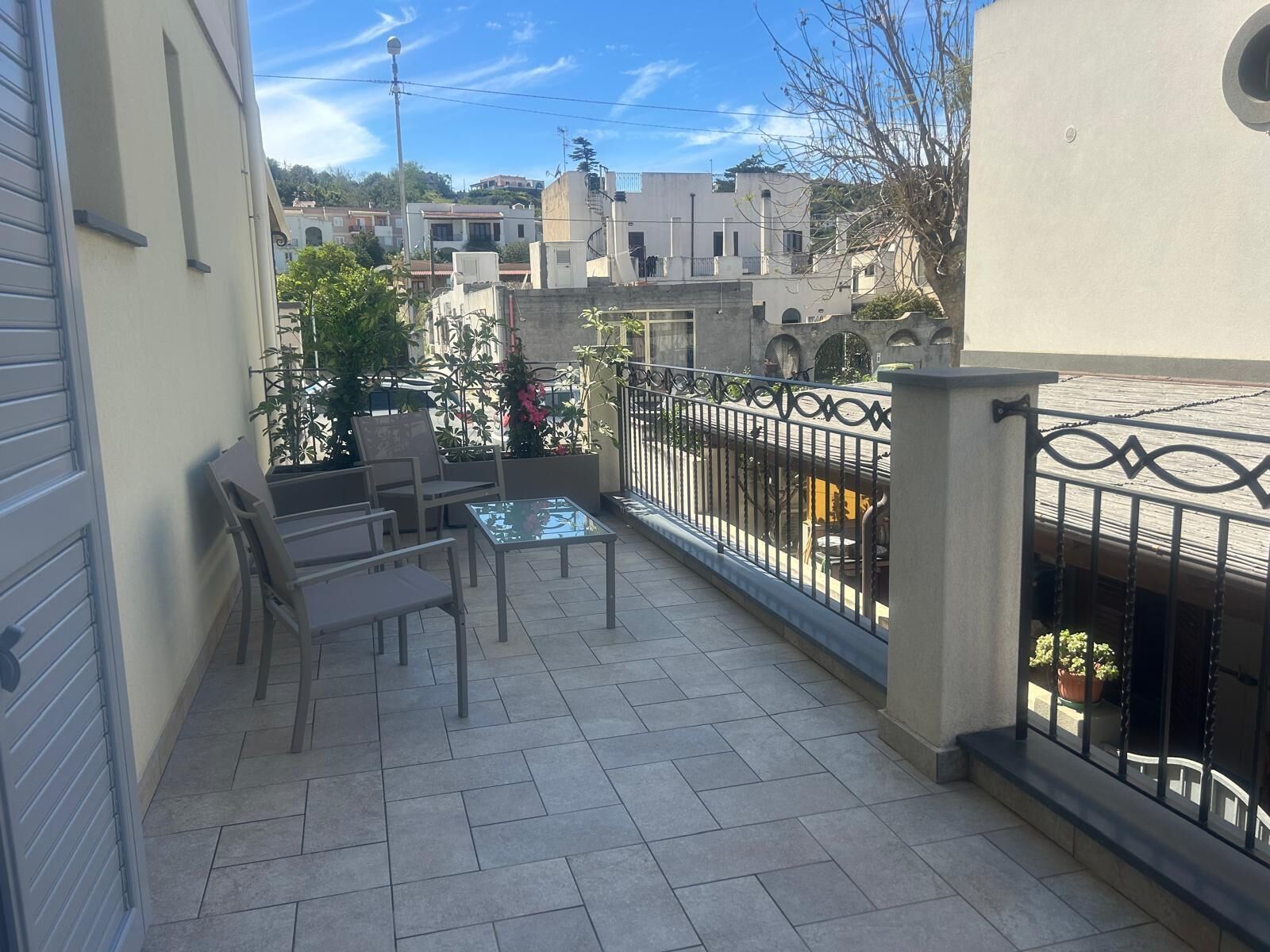Een balkon met betegelde vloer, een glazen tafel en twee stoelen.