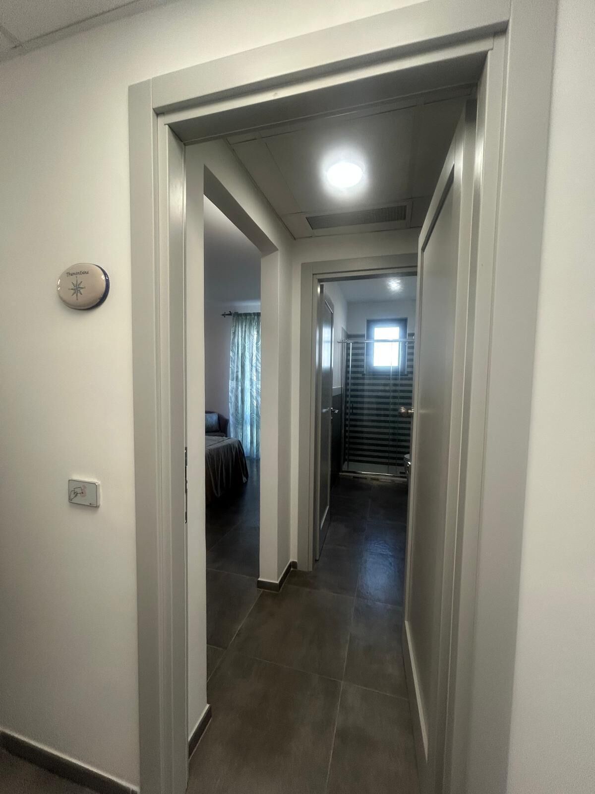 Un pasillo con una puerta que da a un dormitorio con cama y cortinas. Se observa una escalera al fondo.