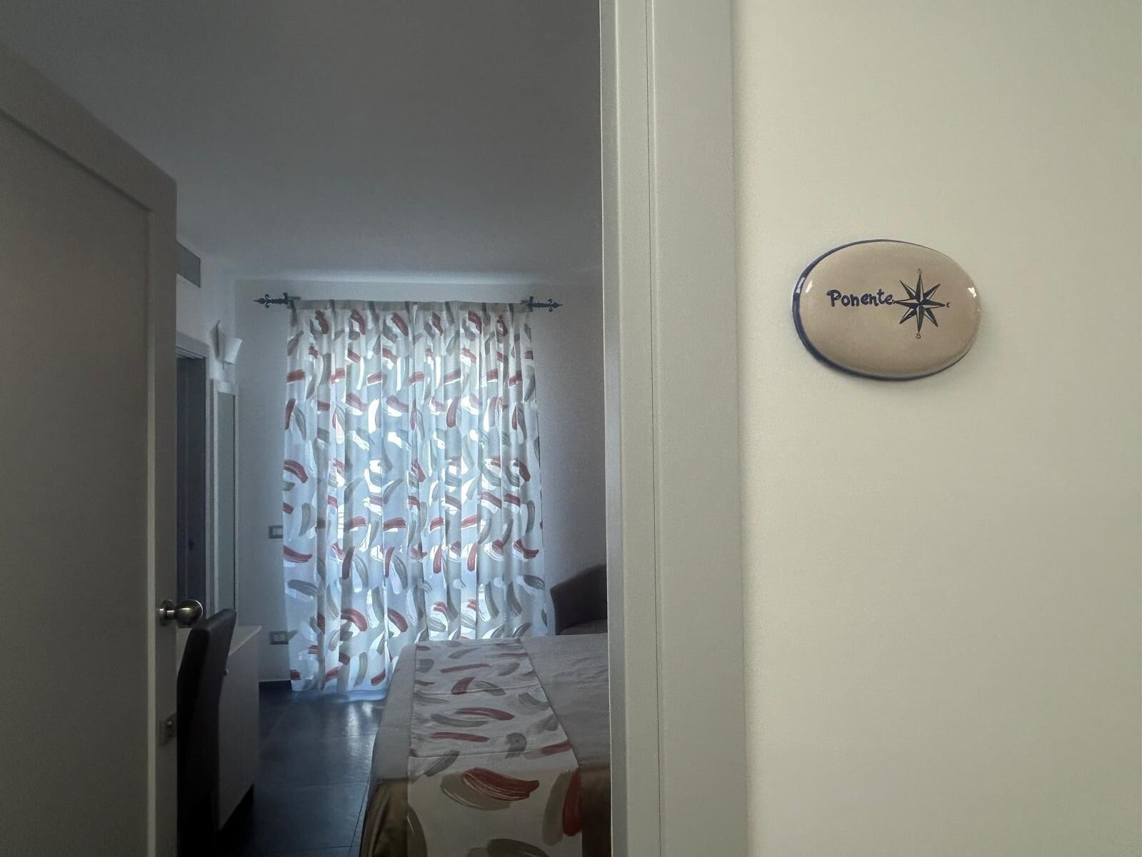 Une chambre d’hôtel avec un lit, un rideau orné de motifs de feuilles et une pancarte sur le mur indiquant « Ponte ».