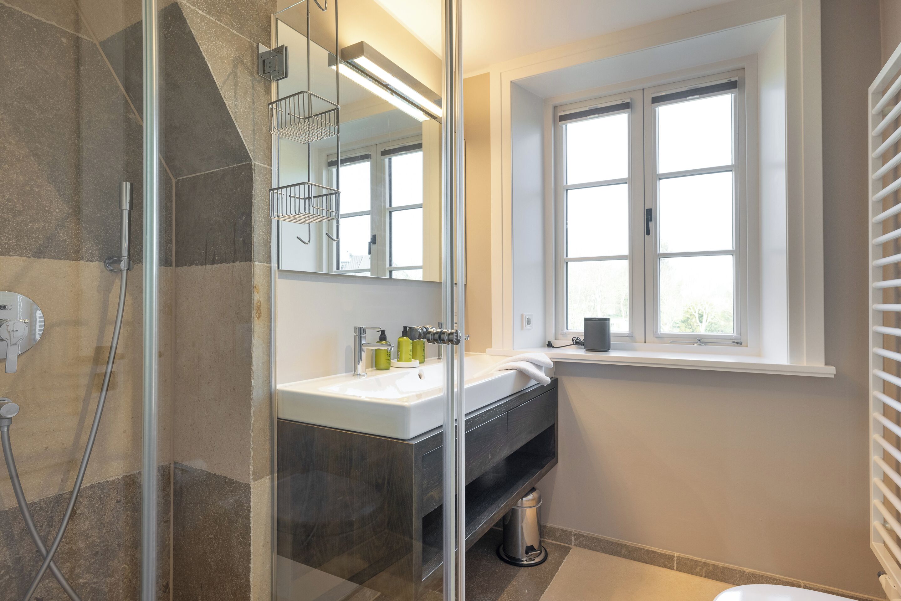 A modern bathroom with a glass shower enclosure, a sink with a mirror above it, and a window providing natural light.