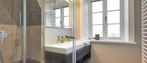 A modern bathroom with a glass shower enclosure, a sink with a mirror above it, and a window providing natural light.