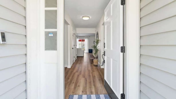 A hallway with white doors, a wooden floor, and a bench with a plant.