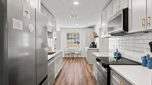 A modern kitchen with stainless steel appliances, white cabinetry, and a wooden floor.