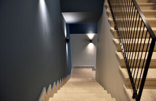 Una escalera con barandilla de metal negro, peldaños color beige y paredes pintadas en azul y blanco.