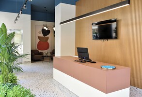 Una recepción con un televisor de pantalla plana, una silla moderna y una mesa pequeña con un cuenco decorativo.