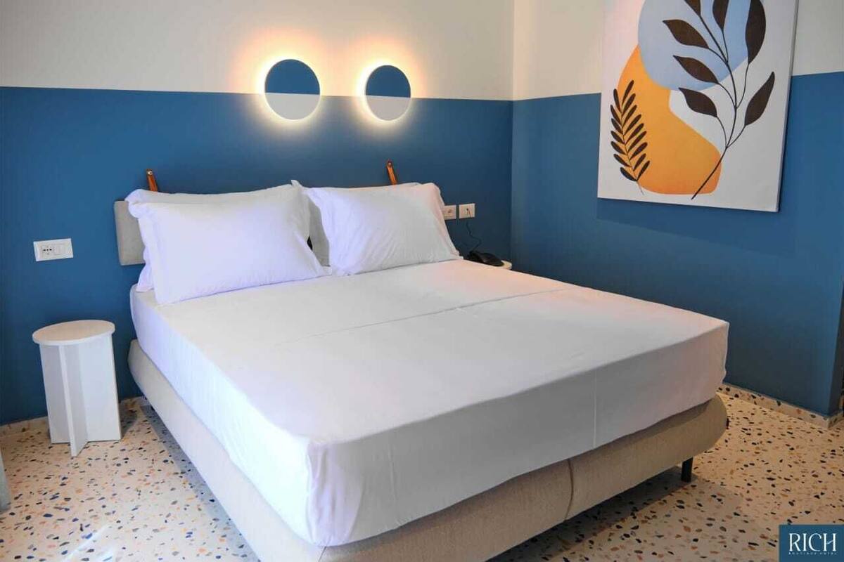 Ein Schlafzimmer mit einem Bett, einem Nachttisch, einer Wandleuchte und einem Gemälde.