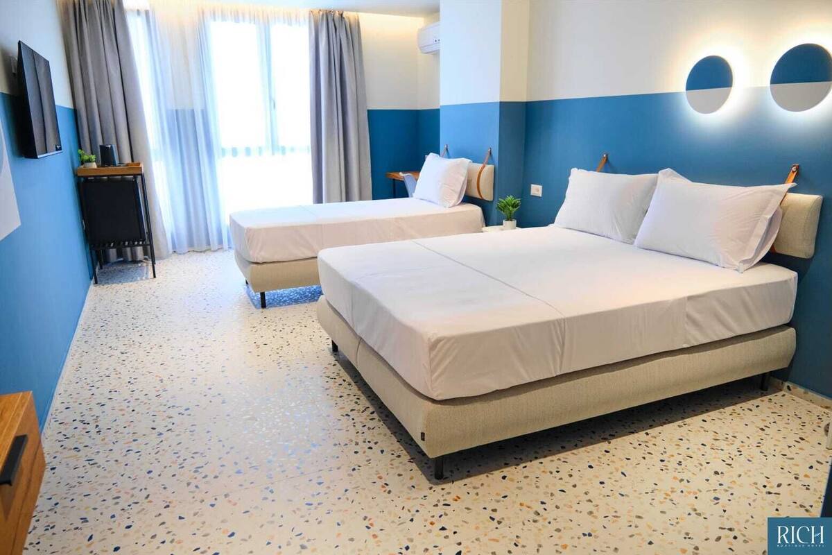 Ein Hotelzimmer mit zwei Betten, einem Fernseher, einem kleinen Tisch und einer Pflanze.