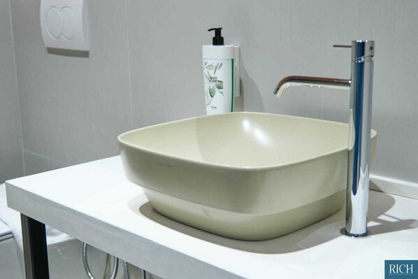 Une salle de bain avec un lavabo blanc, un robinet moderne et un distributeur de savon fixé au mur.