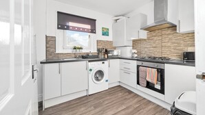 Une cuisine moderne avec des meubles blancs, un lave-linge encastré, un four à micro-ondes et une cuisinière.