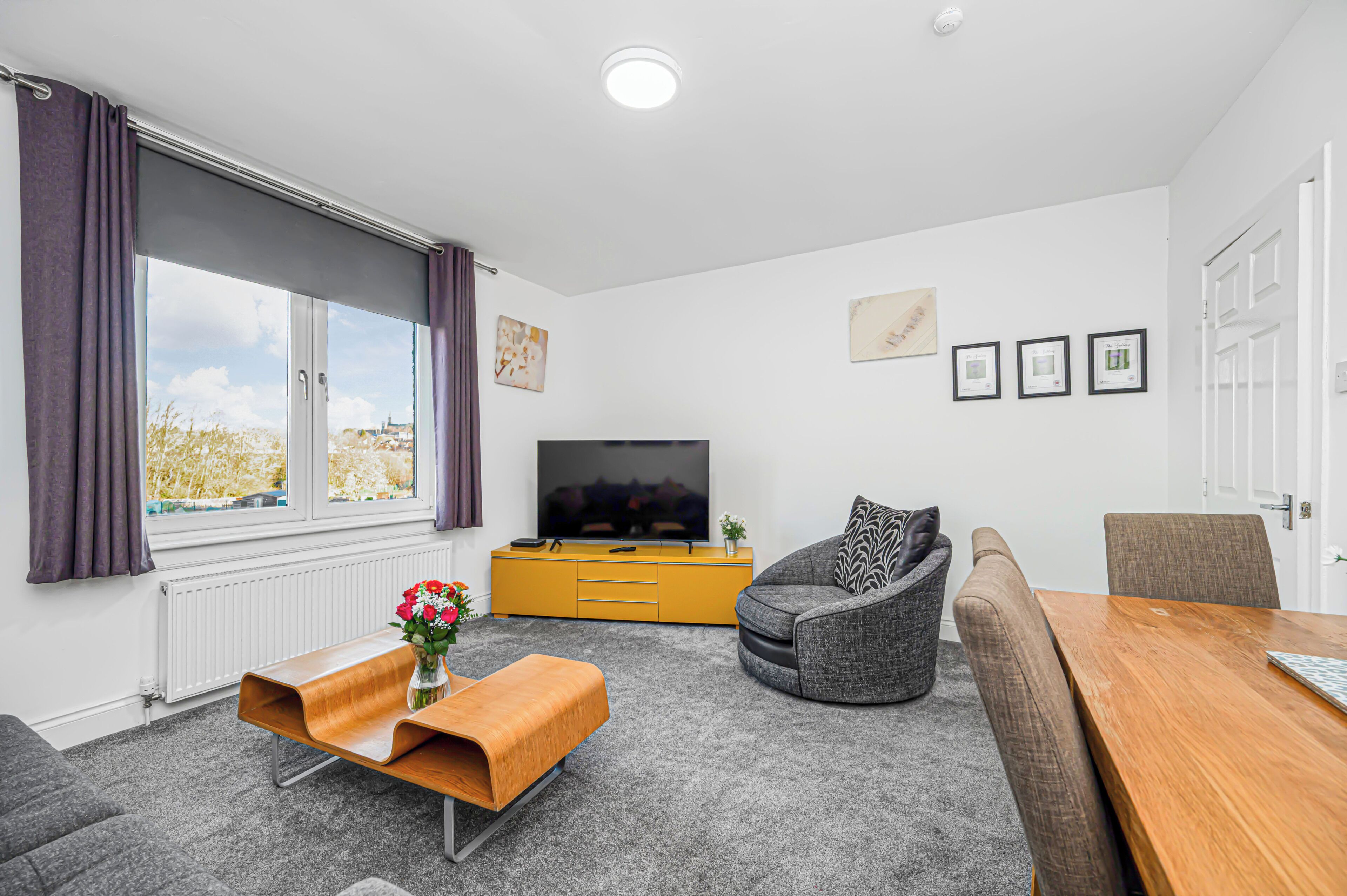 Een moderne woonkamer met een bank, een houten salontafel, een televisie en een eettafel.