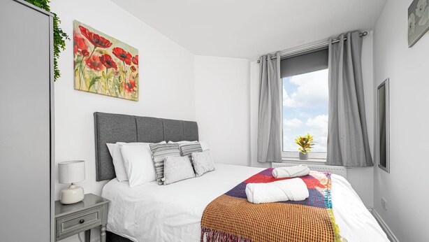 Une chambre bien rangée, avec un lit, une table de chevet, une lampe et une fenêtre avec des rideaux.