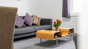 Un salon moderne avec un canapé gris, des coussins violets et une table basse en bois sur laquelle est posé un vase de fleurs.