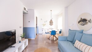 A modern living room with a flat-screen TV, a blue sofa, and a dining area with chairs and a table.