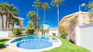 A swimming pool surrounded by palm trees and a white building with balconies.