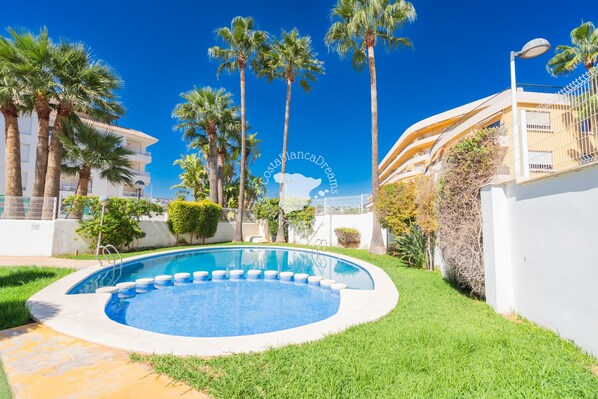 A swimming pool surrounded by palm trees and a white building with balconies.