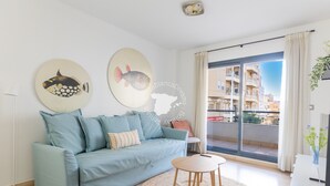 A modern living room with a light blue sofa, a round coffee table, and two wall-mounted fish art pieces.