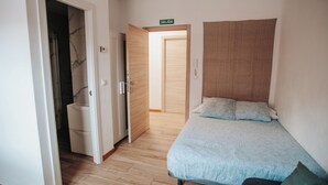 A bedroom with a bed, a wooden door, and a bathroom visible through an open door. - POLOESTUDIOS (Zaratán)