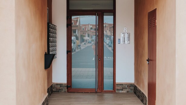 A hallway leading to a door with a number plate, a security camera, and a mailbox on the wall. - POLOESTUDIOS (Zaratán)