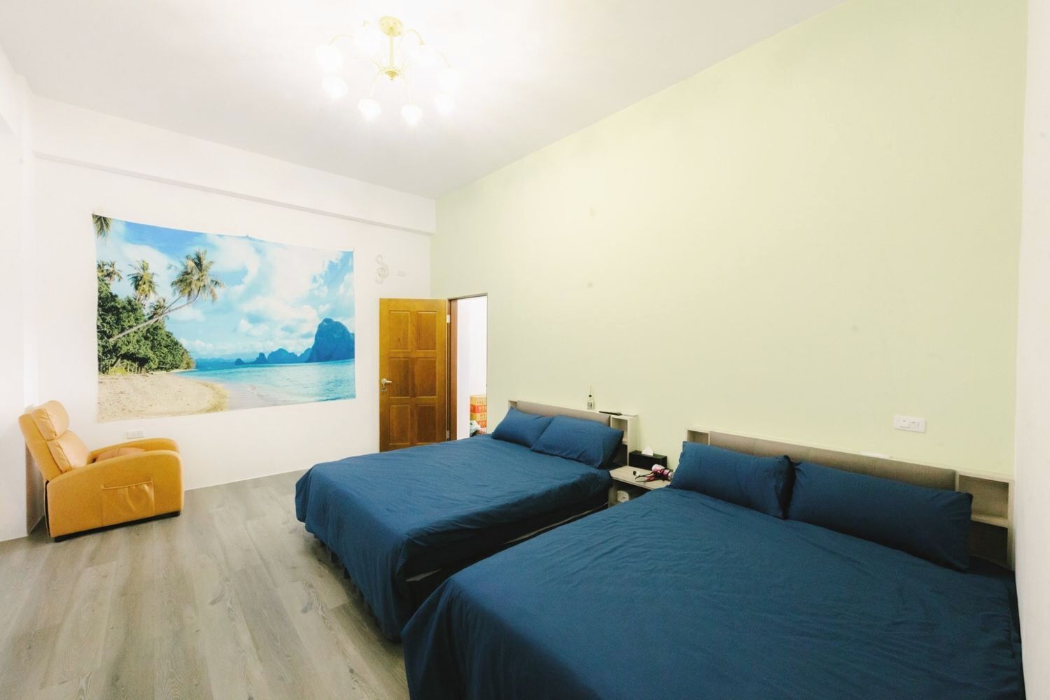 A room with two beds, a chair, and a painting of a beach scene.